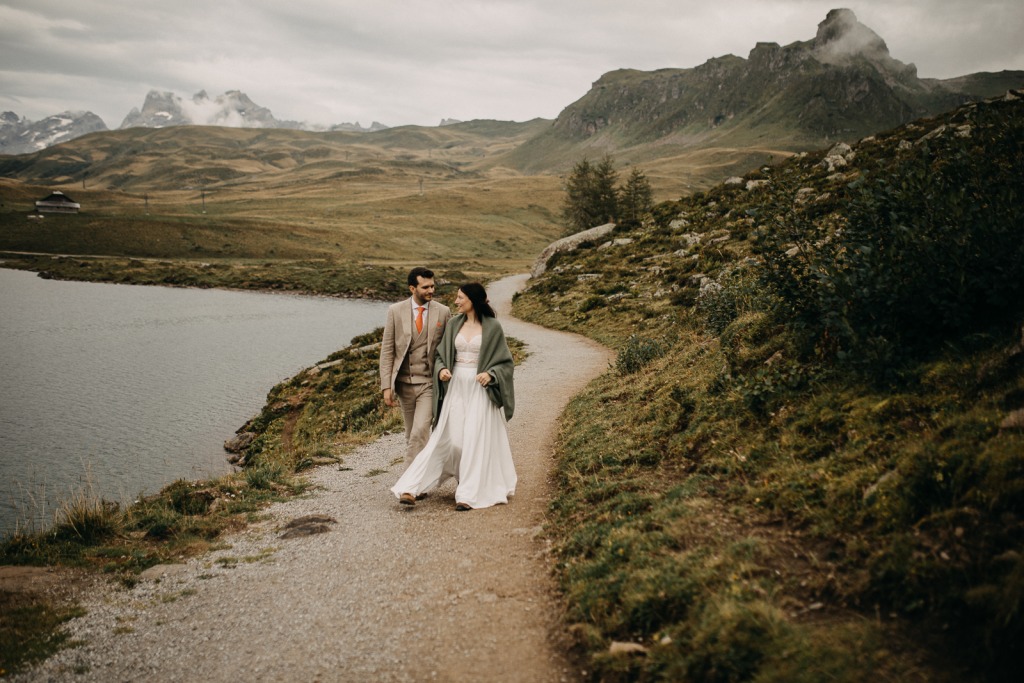 Paar läuft in den Bergen in der Schweiz auf einem schmalen Feldweg und blickt auf den See