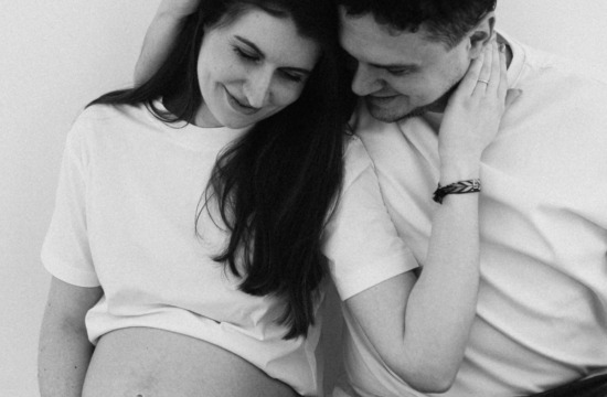 Paaraufnahme in schwarz weiß von einer schwangeren Frau und ihrem Partner, der sie umarmt und sie ihn