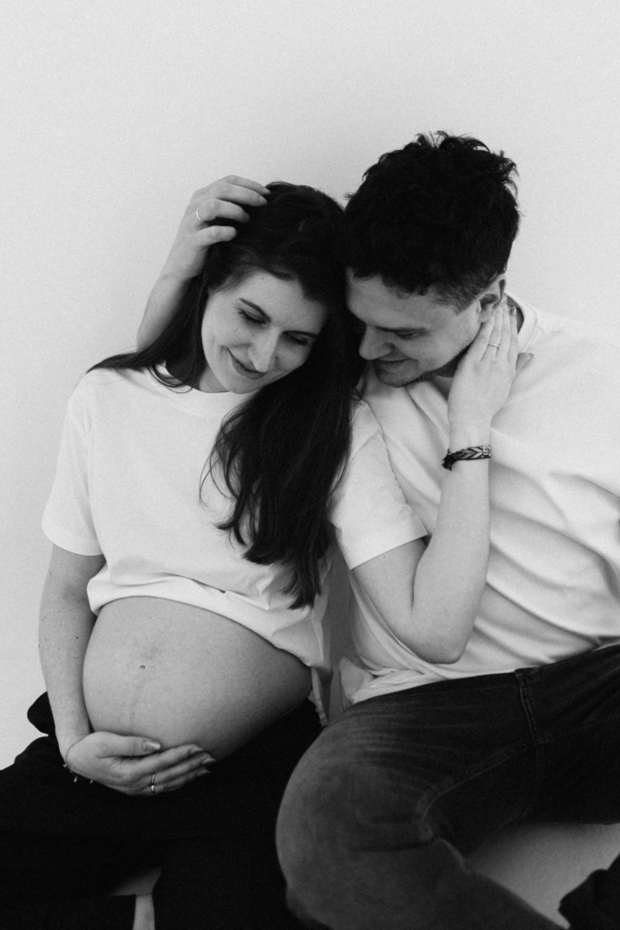 Paaraufnahme in schwarz weiß von einer schwangeren Frau und ihrem Partner, der sie umarmt und sie ihn