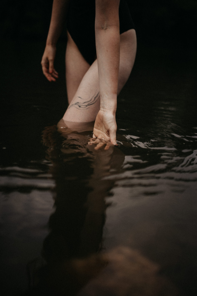 Stimmungsvolle Nahaufnahme von einer Frau, die durch das Wasser geht, man sieht nur die Hand, die durch das Wasser streift