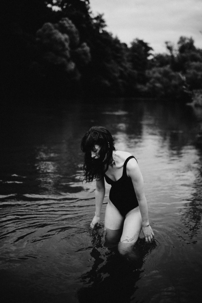 Schwarz weißes künstlerisches und geheimnissvolles Portrait einer langhaarigen Frau im Wasser, die ihre Finger durch das Wasser gleiten lässt