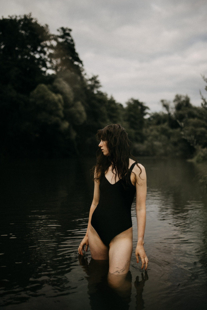Geheimnisvolles Portrait einer dunkelhaarigen Frau, die im Bikini durchs Wasser läuft aber nicht direkt in die Kamera blickt als würde sie etwas suchen