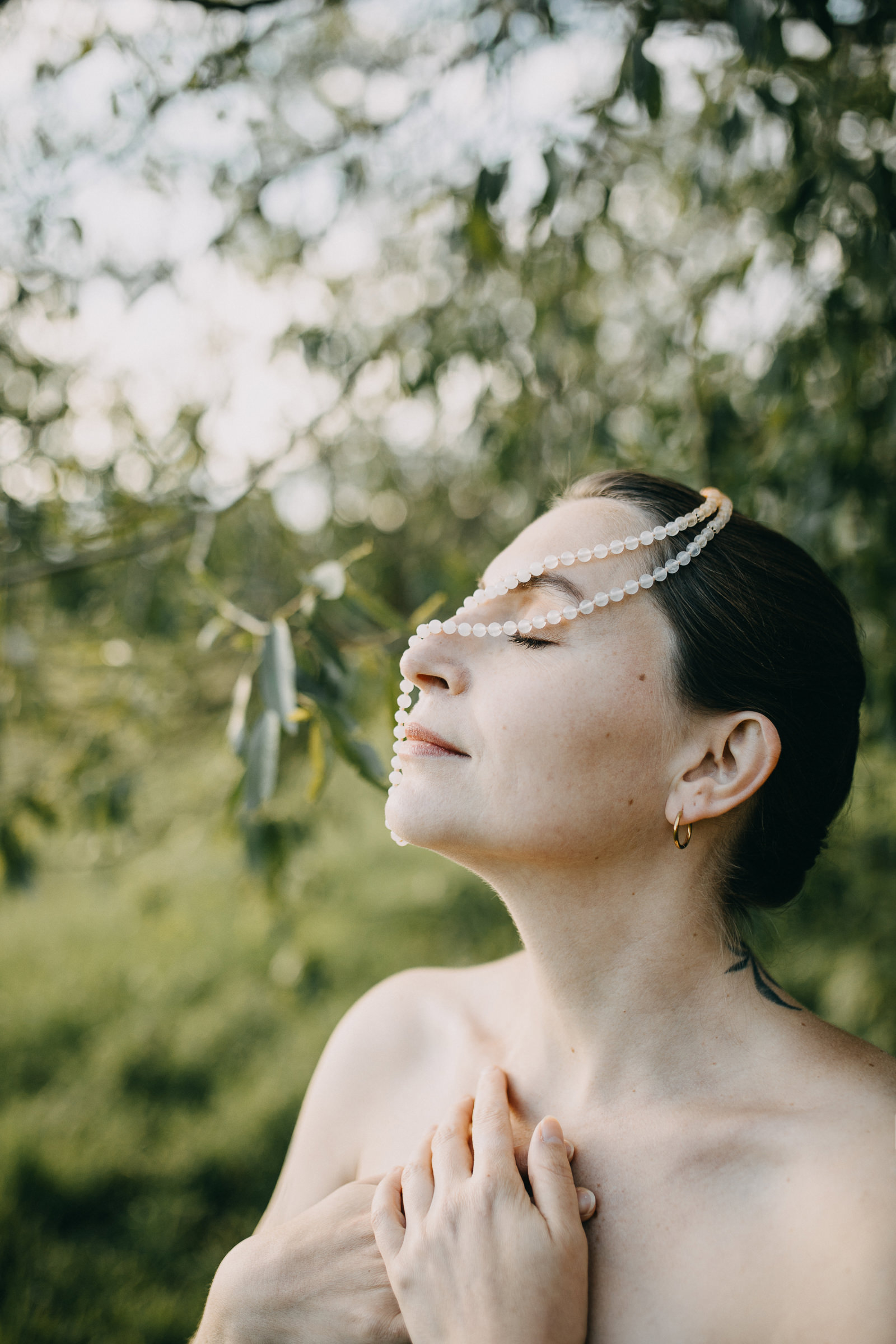 Portrait an einem Frühlingsabend von der Yogalehrerin Elisa von Körpergefühl mit einer Malakette über das Gesicht geschlungen, die Hände über der Brust überkreuzt.
