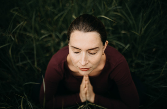 Portrait von Elisa Körperfefühl mit geschlossenen Augen und aufeinandergelegten Händen im Gras sitzend für ein Yogashooting