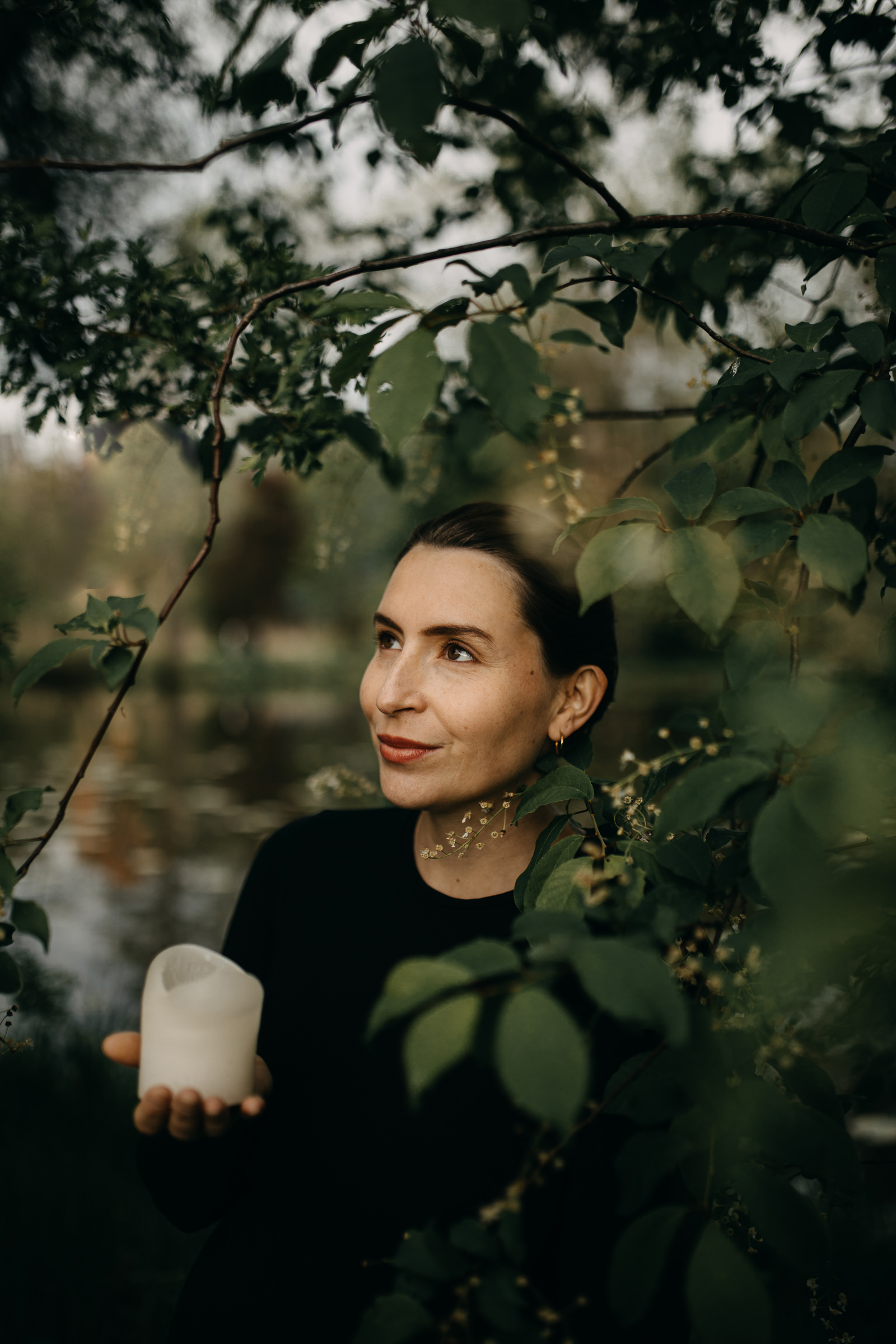 Portrait von der Yogalehrerin Elisa Körpergefühl, zwischen Bäumen stehend mit einer Kerze in der Hand