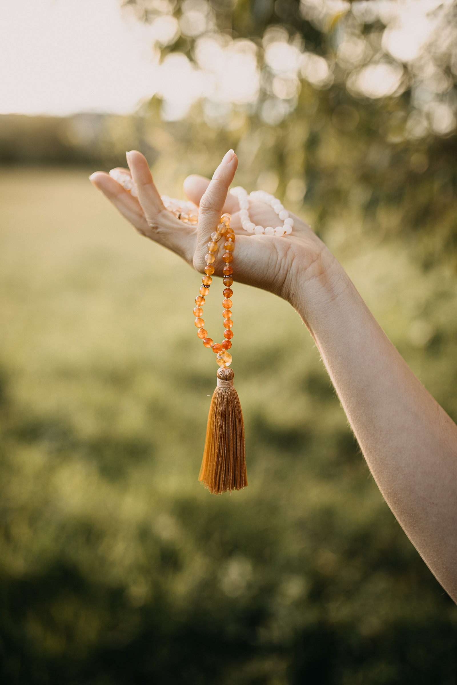 Aufnahme einer Hand, die eine Malakette hält, der Hintergrund ist sommerlich und verschwommen.